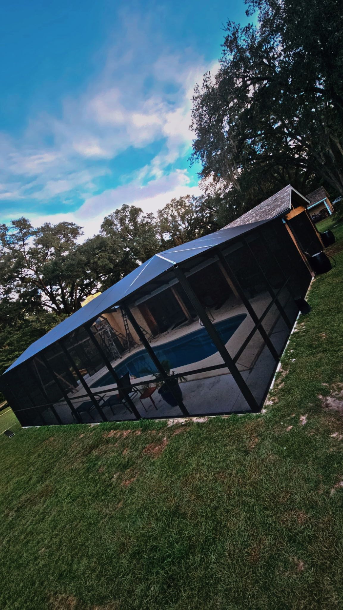 Screened pool enclosure seen from the lawn, with a solid roof section where it meets the house