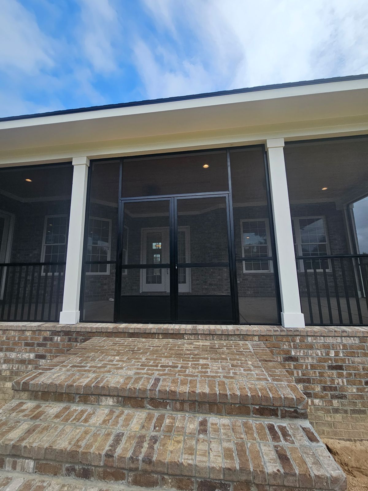 Front porch screened in with black frames, black double screen doors and brick steps