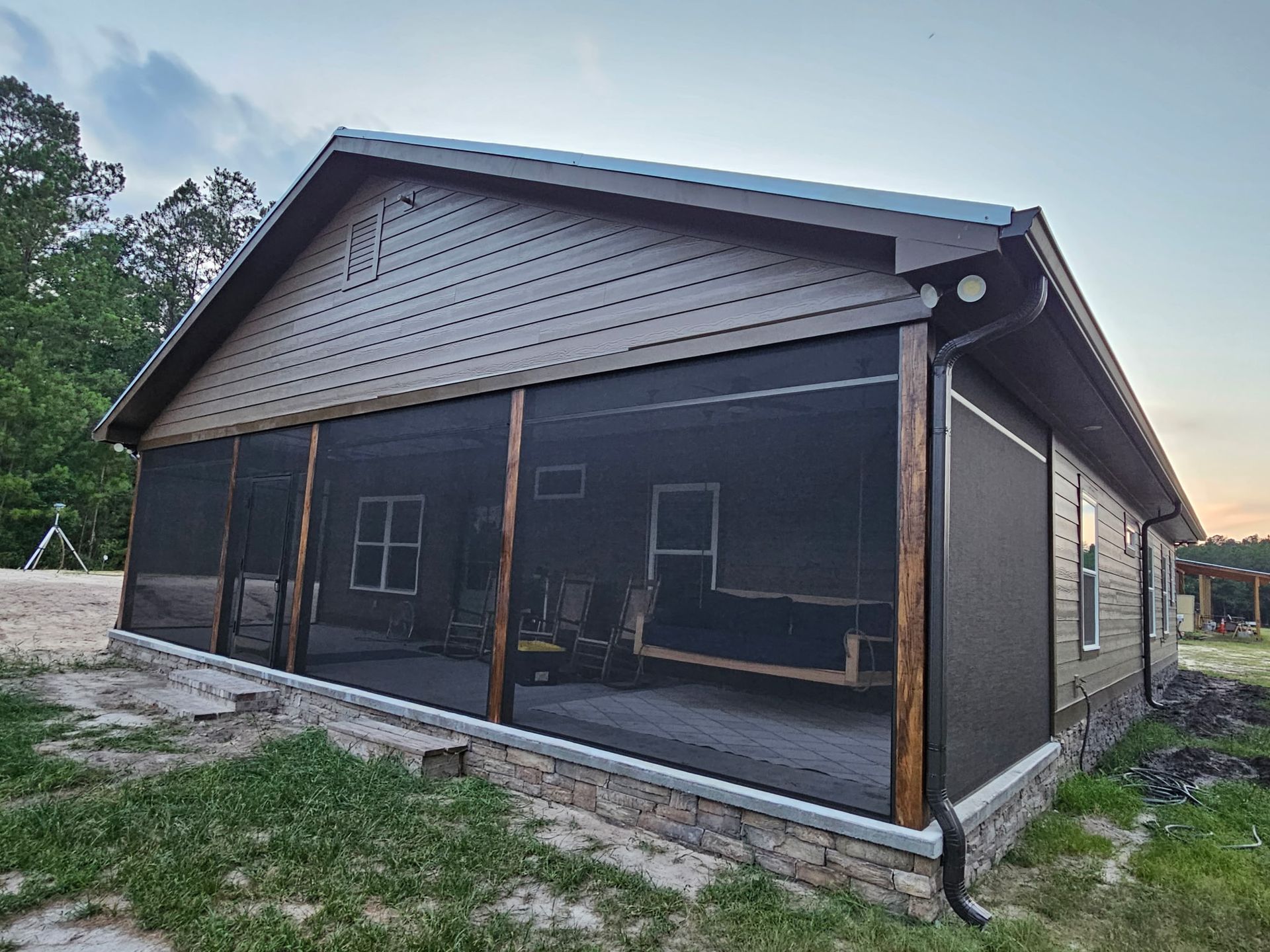 Screen room under a gable roof with a stacked-stone knee wall, dark screen panels and matching dark gutters
